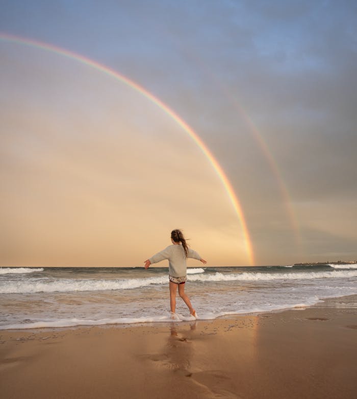 Anonymous woman on beach with rainbow